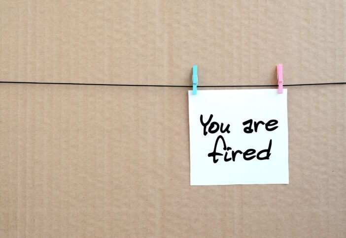 small white sign that says you are fired on cardboard background