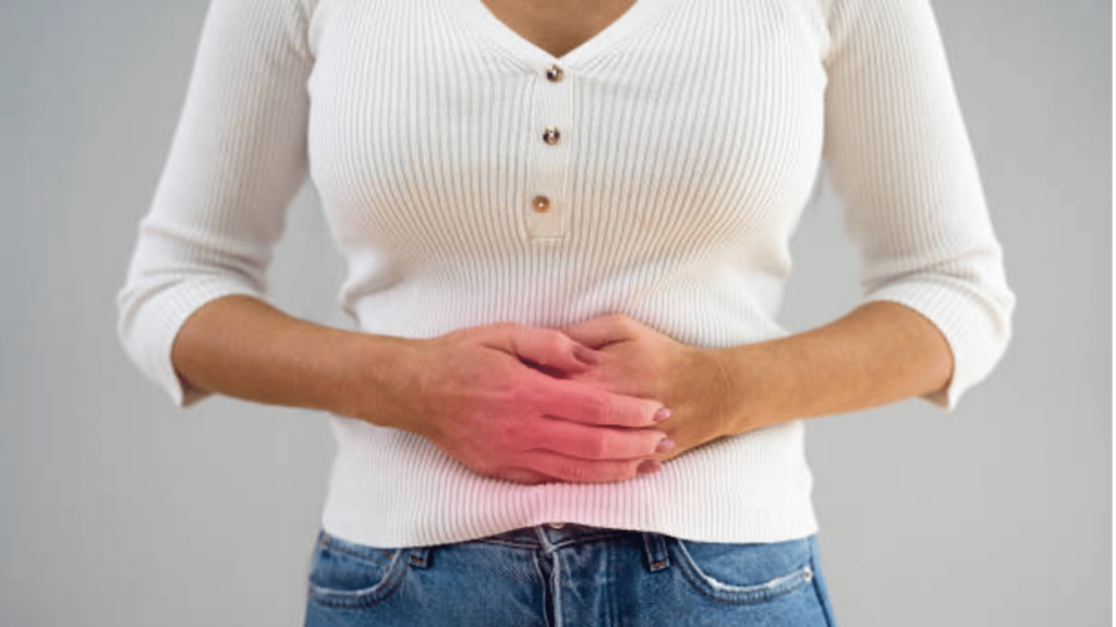 A person wearing a white long-sleeve shirt and jeans can be seen holding his or her hands over their upper abdominal area. There is a red glow over the individual's hands to indicate that the individual is experiencing pain here.