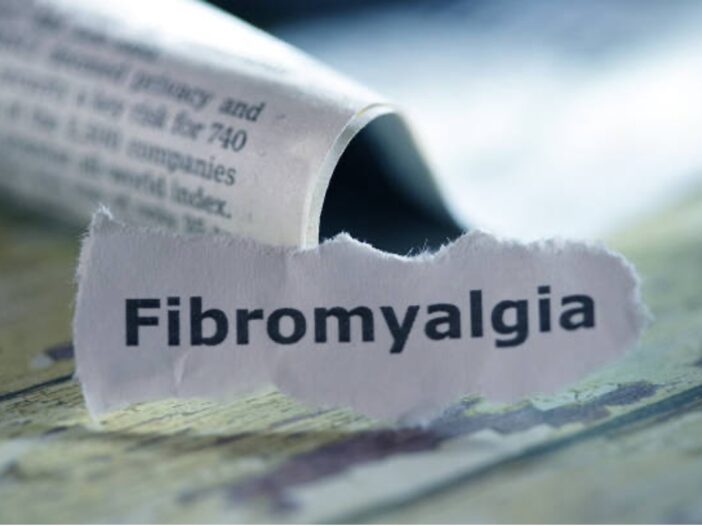 A newspaper cut-out of the word Fibromyalgia can be seen on a wooden surface.