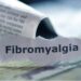 A newspaper cut-out of the word Fibromyalgia can be seen on a wooden surface.