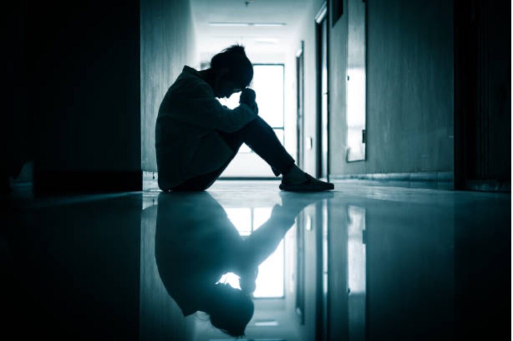 Social Security Disability for Anxiety. A woman sits on the floor of a hallway with her knees tucked while her head faces down.