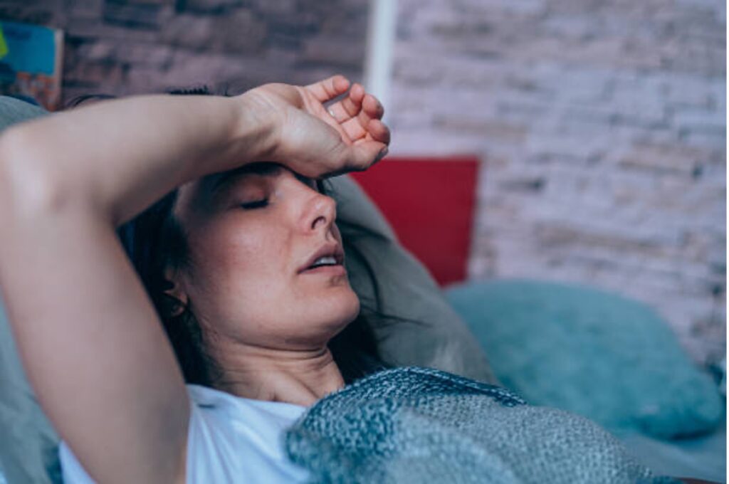 Woman lying down on a couch holds her right hand over her forehead.