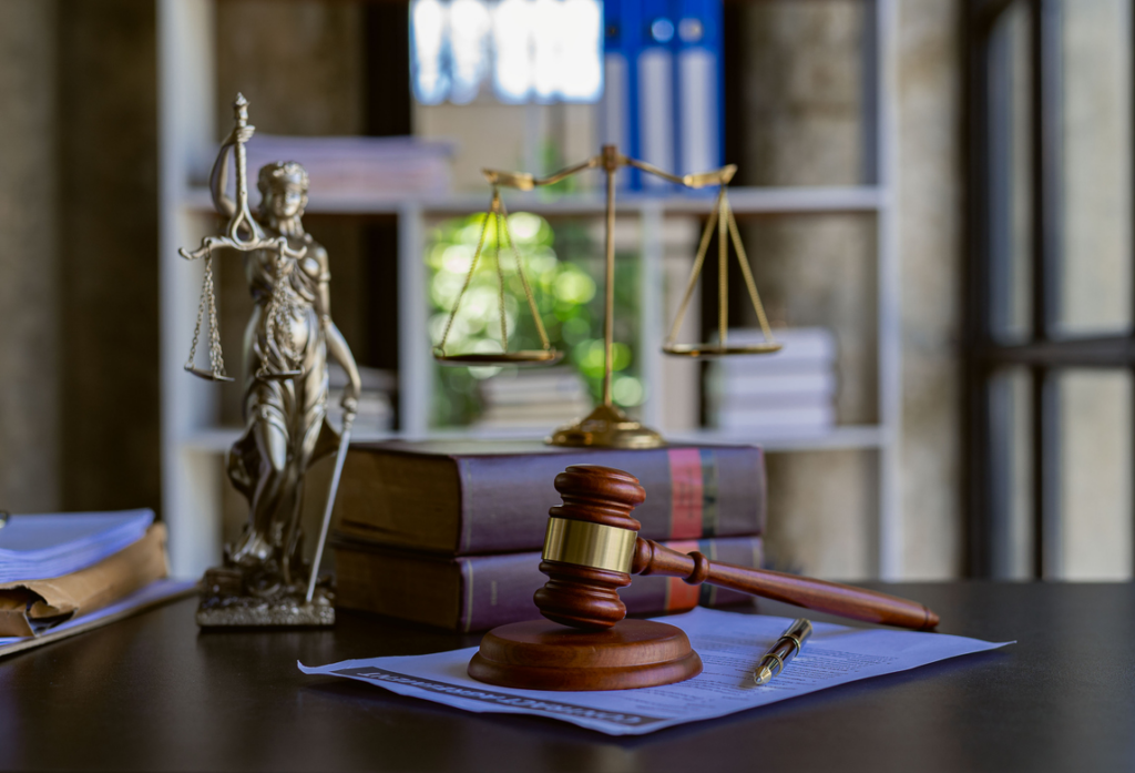 Gavel, statue of justice, and scales of justice on top of books all sitting on top of a desk
