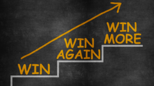 Blackboard with chalk that draws an arrow with steps that say 'win', 'win again', 'win more'