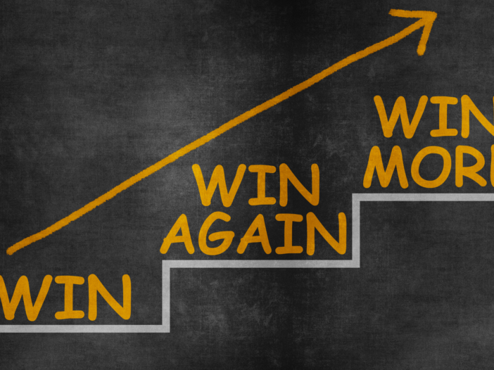 Blackboard with chalk that draws an arrow with steps that say 'win', 'win again', 'win more'