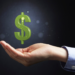 A Caucasian business person's hand, visible from the elbow down in a light blue business shirt cups their hand. A great dollar sign is floating above the hand.