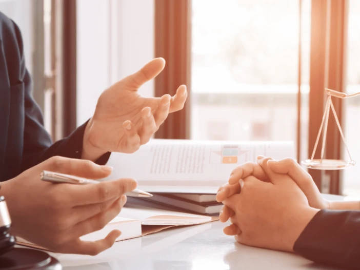 Two people with hands shown sitting at a desk with paperwork conducting legal busines.