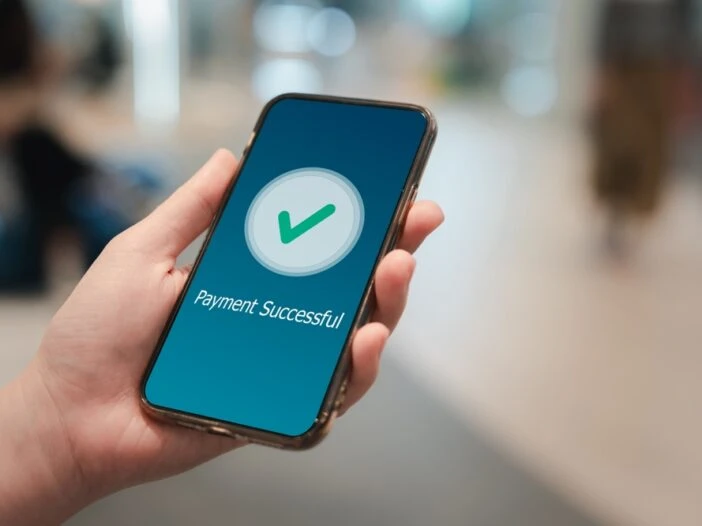 Hand holding a phone with 'payment successful' icon. Title of blog post is "How Much Does SSDI Pay in North Carolina? (Winston-Salem Guide)