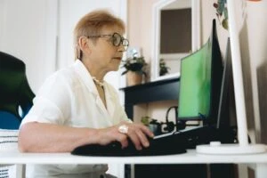 Older female worker sitting at a desk, looking at her computer. This is the header image for a blog post entitled, "Can You Get Disability While Working in Charlotte, NC?"