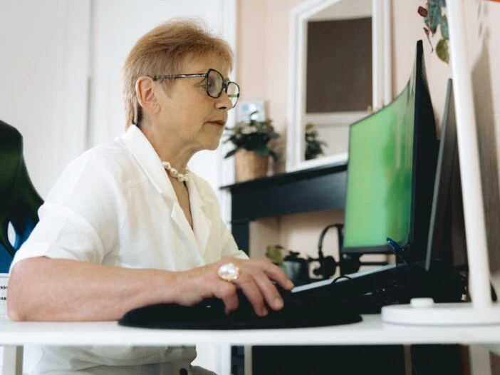 Older female worker sitting at a desk, looking at her computer. This is the header image for a blog post entitled, "Can You Get Disability While Working in Charlotte, NC?"