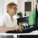 Older female worker sitting at a desk, looking at her computer. This is the header image for a blog post entitled, "Can You Get Disability While Working in Charlotte, NC?"