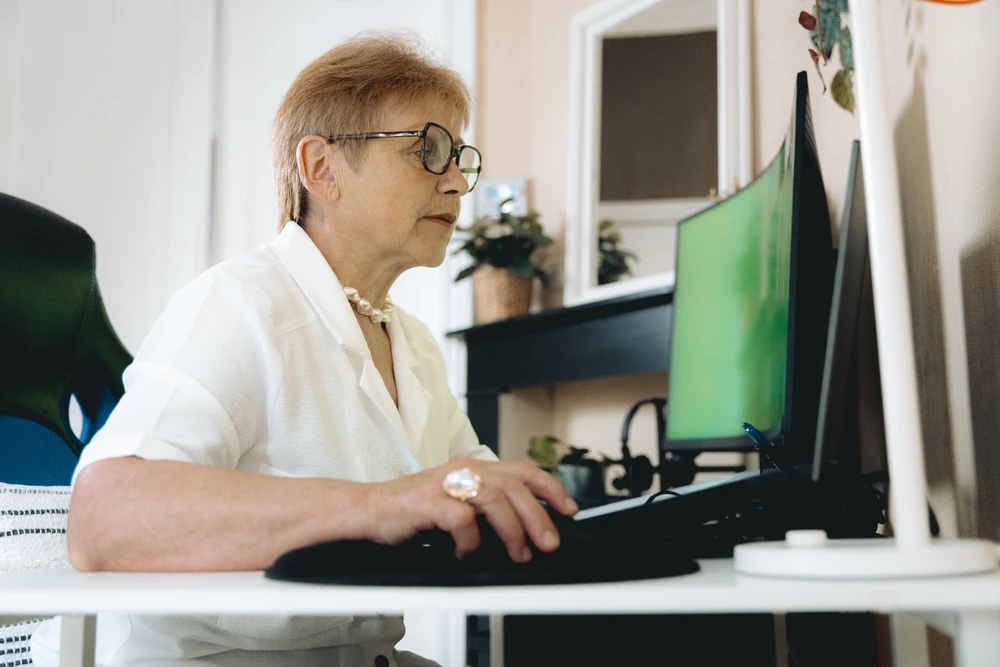Older female worker sitting at a desk, looking at her computer. This is the header image for a blog post entitled, "Can You Get Disability While Working in Charlotte, NC?"