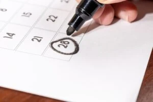 A calendar with a black marker held by a hand and a circle around the date of the 28th. This image is the header image of a blog post titled - What Is Date Last Insured in a North Carolina Disability Claim?