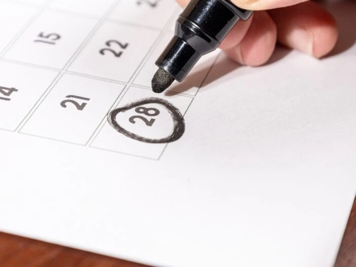 A calendar with a black marker held by a hand and a circle around the date of the 28th. This image is the header image of a blog post titled - What Is Date Last Insured in a North Carolina Disability Claim?