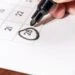 A calendar with a black marker held by a hand and a circle around the date of the 28th. This image is the header image of a blog post titled - What Is Date Last Insured in a North Carolina Disability Claim?
