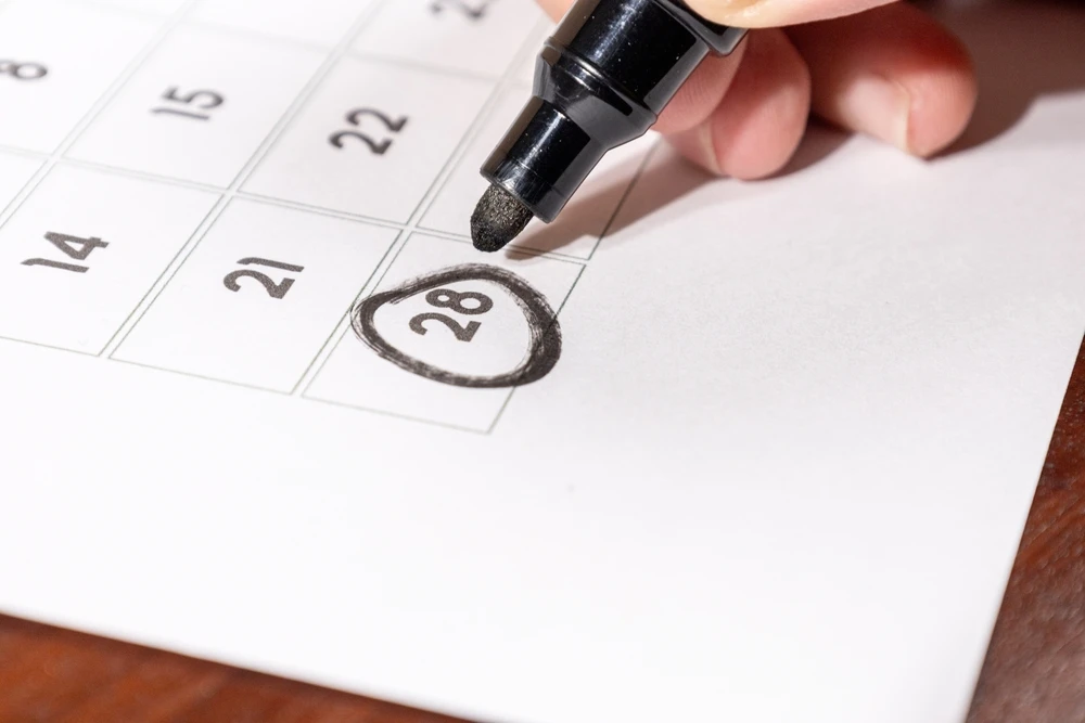 A calendar with a black marker held by a hand and a circle around the date of the 28th. This image is the header image of a blog post titled - What Is Date Last Insured in a North Carolina Disability Claim?