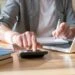 Picture of a man at a computer with a calculator making calculations. This image is the header image for a blog post titled - What Are Work Credits for Social Security Disability in North Carolina?