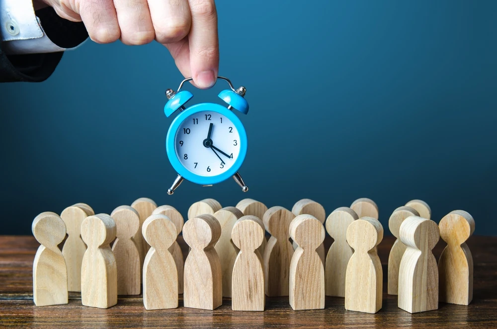 A,Businessman,Is,Holding,An,Alarm,Clock,Over,A,Crowd in this image that accompanies the blog post about Trial Work Periods and Social Security Disability