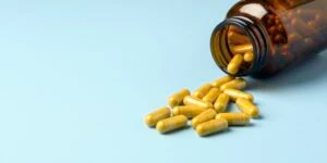 A picture of pills spilling out from an amber bottle onto a blue background which is the header image for a blog post titled: How Medication Side Effects Can Affect a Social Security Disability Claim in North Carolina