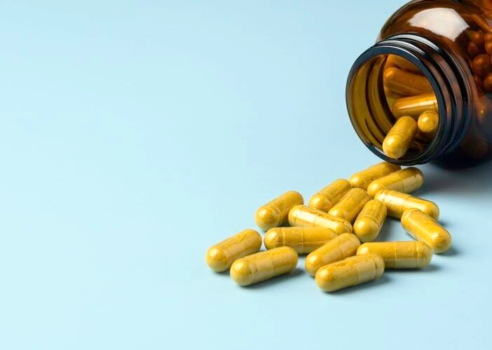 A picture of pills spilling out from an amber bottle onto a blue background which is the header image for a blog post titled: How Medication Side Effects Can Affect a Social Security Disability Claim in North Carolina