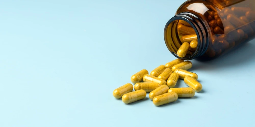 A picture of pills spilling out from an amber bottle onto a blue background which is the header image for a blog post titled: How Medication Side Effects Can Affect a Social Security Disability Claim in North Carolina