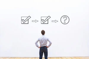 A business man staring at a white board with two checkmarks and a third step marked with a question mark. This is the header image accompanying a blog post titled - What Happens After a Trial Work Period for Social Security Disability in North Carolina?